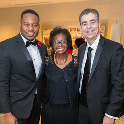 Photograph of two smiling men in suits and a smiling woman standing together