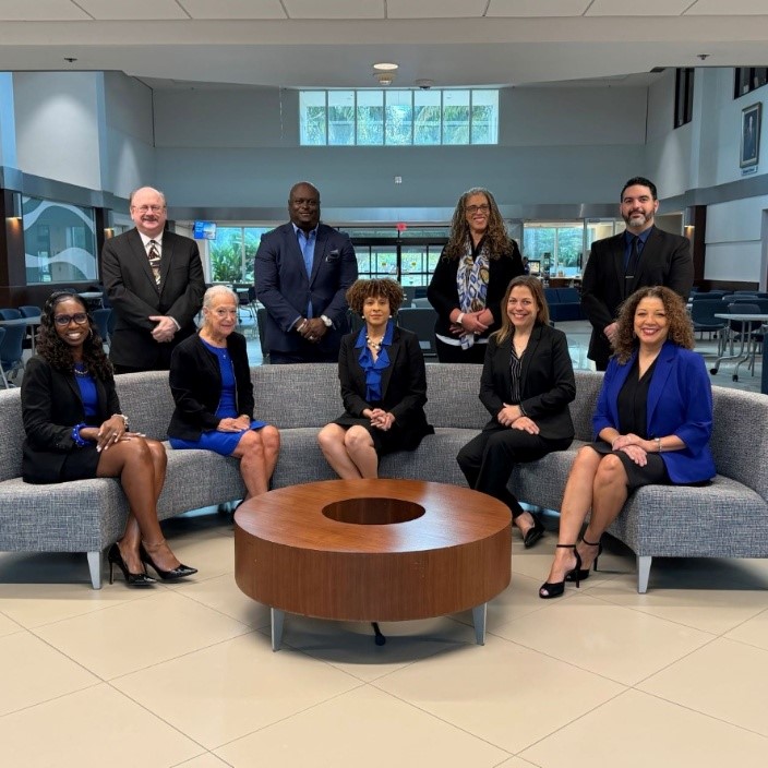 Group picture of smiling adults sitting on a gray couch and posing behind the couch
